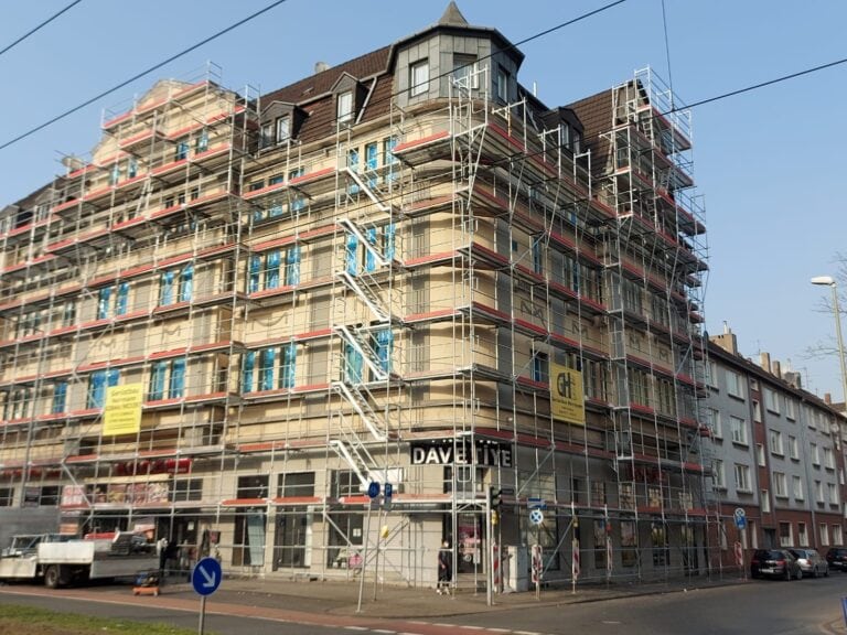 Ein vierstöckiges Gebäude mit Gerüst, blauer Himmel, Baustellenschilder, Ecke einer Stadtstraße.