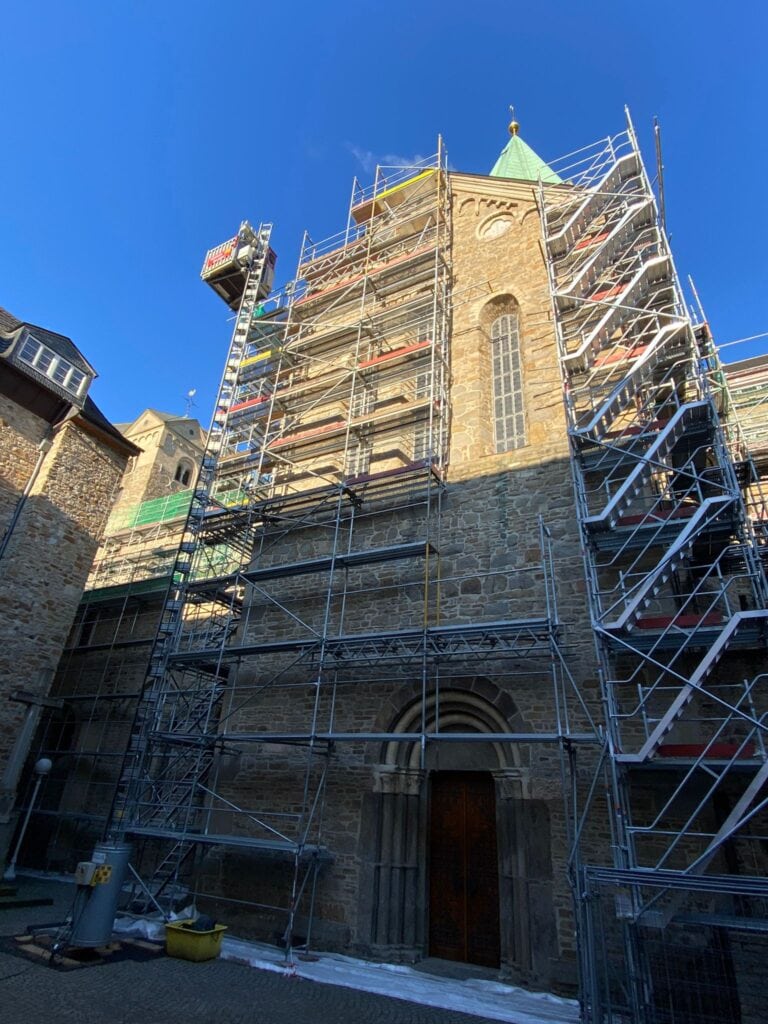 Gerüst an steinerner Kirche mit spitzem Turm; blauer Himmel; Restaurierung im Gange.